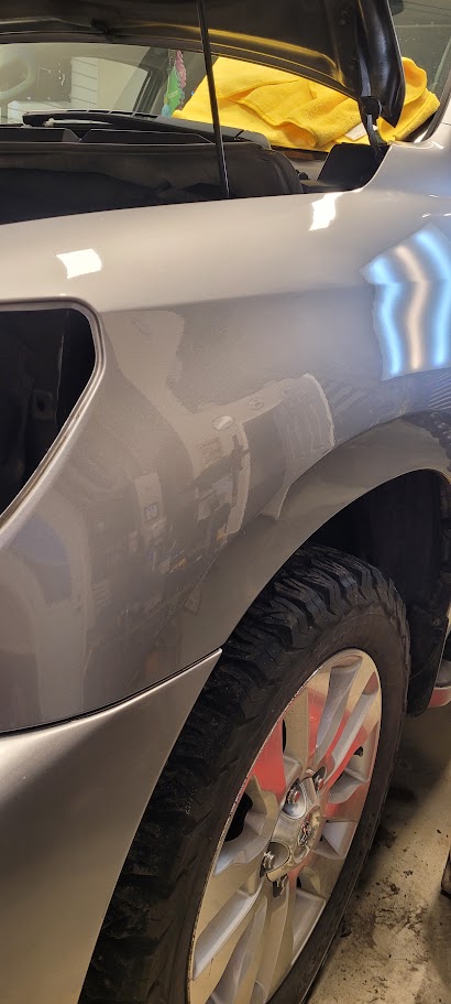 Silver vehicle fender with dents marked by green PDR tabs before repair